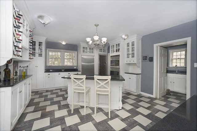 kitchen featuring white cabinets, dark countertops, appliances with stainless steel finishes, a chandelier, and a kitchen island