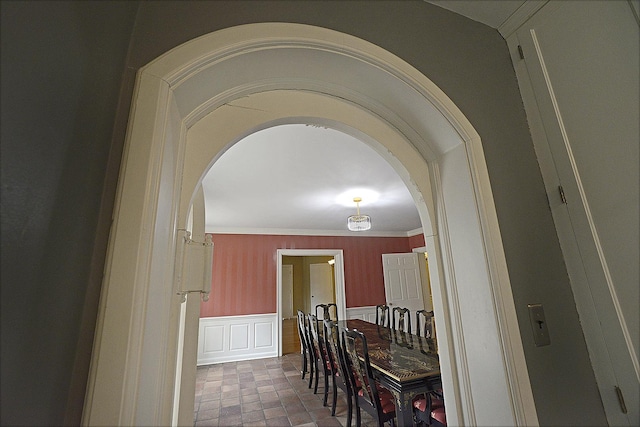 dining room featuring arched walkways, ornamental molding, and a wainscoted wall