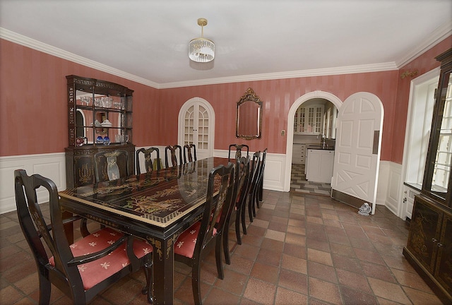 dining room featuring crown molding, arched walkways, wainscoting, and a decorative wall