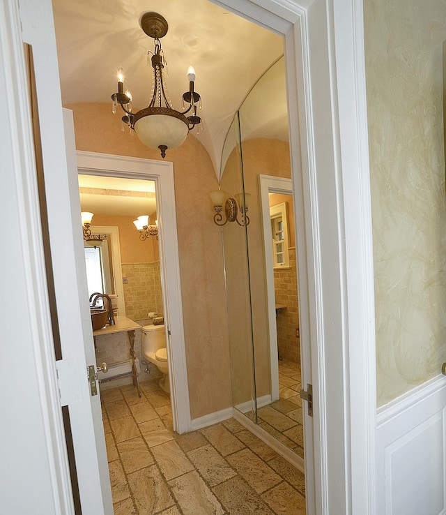 bathroom featuring lofted ceiling, toilet, stone tile flooring, and a notable chandelier