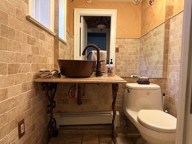 bathroom with a sink, baseboard heating, toilet, and tile walls