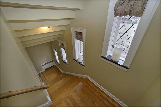 stairway with wood finished floors, baseboards, and a baseboard heating unit