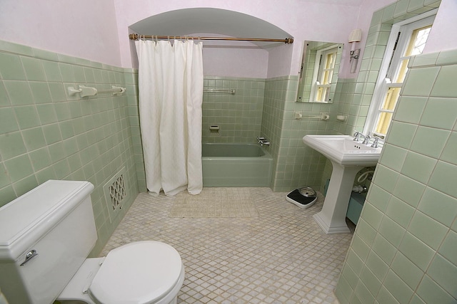 full bath featuring tile walls, a wainscoted wall, shower / bath combo, and toilet