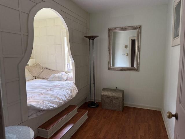 bedroom featuring arched walkways, baseboards, and dark wood-style floors