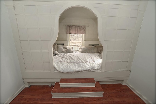 bedroom featuring baseboards, arched walkways, and wood finished floors