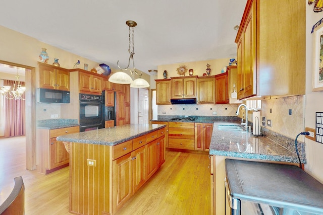 kitchen featuring a kitchen island, decorative light fixtures, sink, black appliances, and light hardwood / wood-style flooring