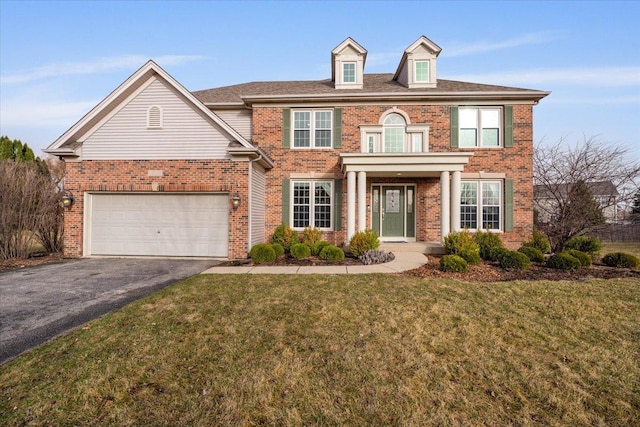 colonial inspired home with a garage, aphalt driveway, a front lawn, and brick siding