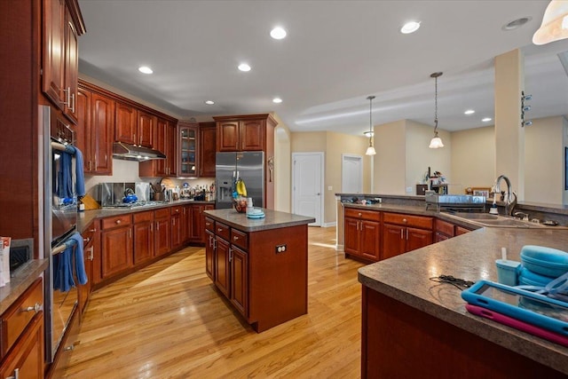 kitchen featuring dark countertops, appliances with stainless steel finishes, a spacious island, a sink, and light wood-style floors