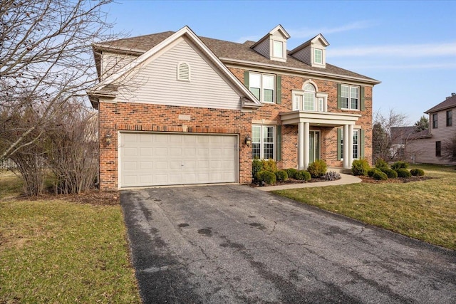 colonial inspired home with aphalt driveway, brick siding, a garage, and a front lawn