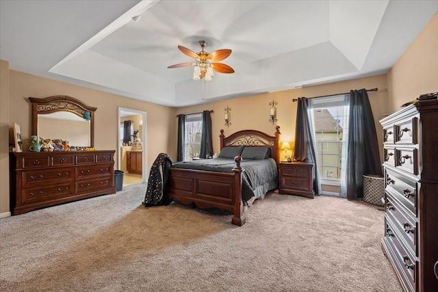 bedroom with ensuite bathroom, a raised ceiling, multiple windows, and light carpet