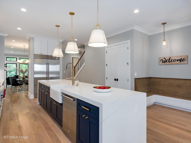 kitchen featuring sink, appliances with stainless steel finishes, hanging light fixtures, a center island with sink, and blue cabinets