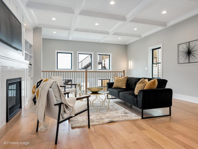 living room featuring coffered ceiling, a tiled fireplace, light hardwood / wood-style flooring, and beamed ceiling