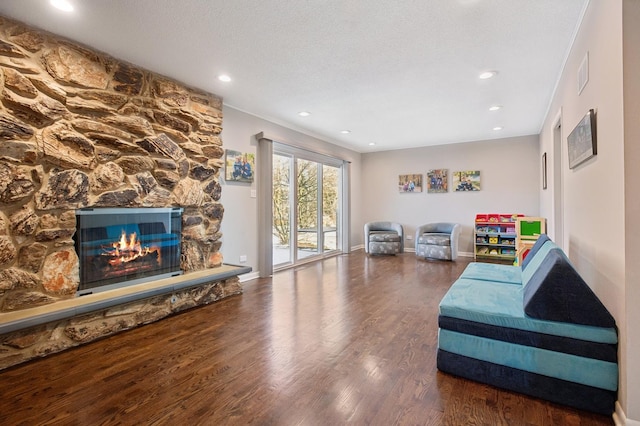 living area featuring a stone fireplace, a textured ceiling, and dark hardwood / wood-style flooring