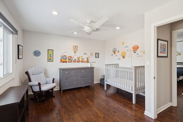 bedroom featuring dark wood-type flooring, a crib, and ceiling fan