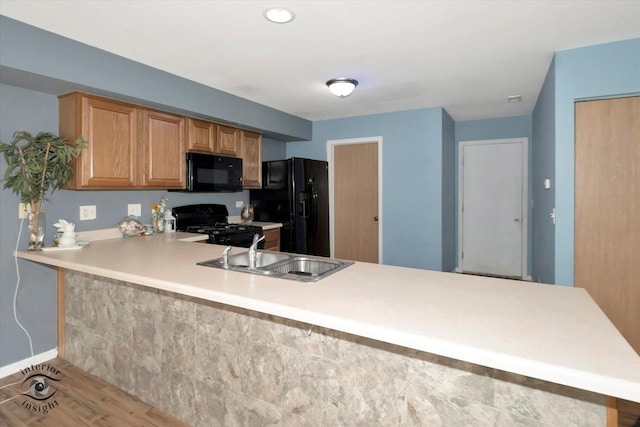kitchen with light countertops, a sink, baseboards, black appliances, and a peninsula