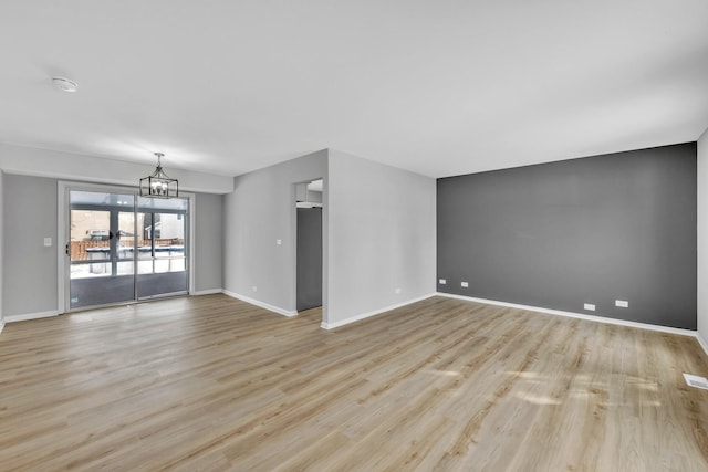 spare room with an inviting chandelier and light wood-type flooring