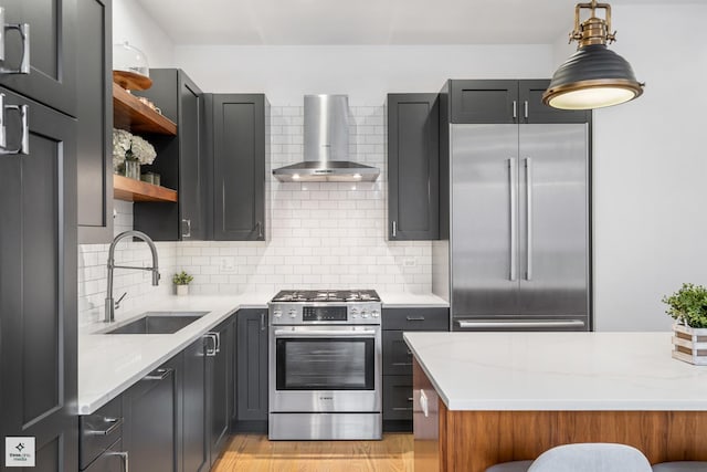 kitchen with wall chimney range hood, sink, stainless steel appliances, tasteful backsplash, and light stone countertops