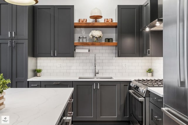 kitchen featuring sink, light stone counters, appliances with stainless steel finishes, decorative backsplash, and wall chimney range hood