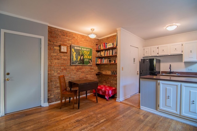 kitchen with sink, white cabinetry, fridge, hardwood / wood-style flooring, and brick wall