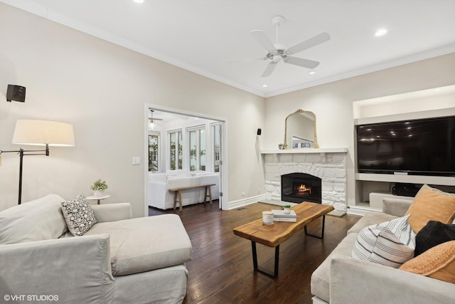 living room featuring ornamental molding, a stone fireplace, dark wood-type flooring, and ceiling fan