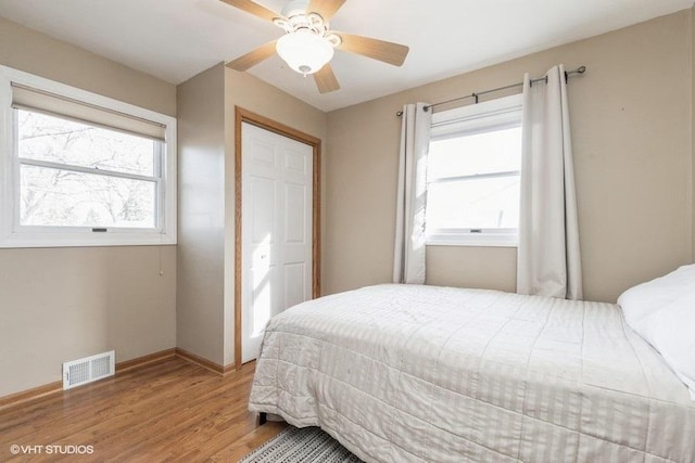 bedroom with hardwood / wood-style flooring, a closet, ceiling fan, and multiple windows