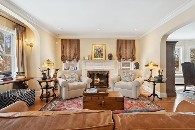 living area with ornamental molding, a brick fireplace, and wood-type flooring