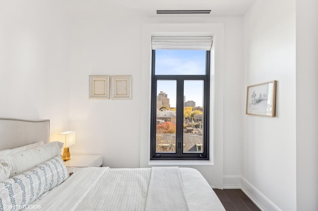 bedroom featuring a view of city, dark wood-type flooring, and baseboards