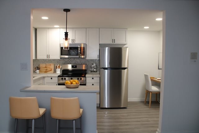 kitchen featuring pendant lighting, a breakfast bar area, white cabinetry, stainless steel appliances, and decorative backsplash