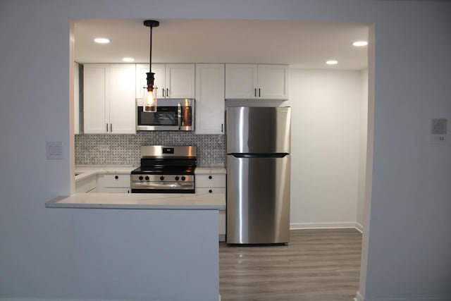 kitchen with pendant lighting, white cabinetry, appliances with stainless steel finishes, kitchen peninsula, and hardwood / wood-style flooring