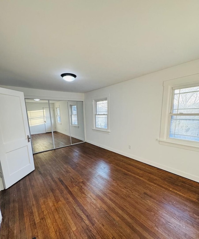 unfurnished bedroom featuring multiple windows, dark hardwood / wood-style floors, and a closet