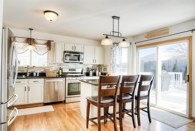 kitchen featuring stainless steel appliances, white cabinetry, a breakfast bar, and decorative light fixtures