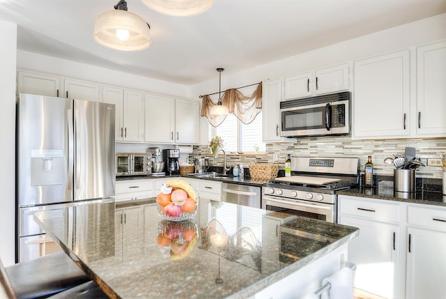 kitchen with white cabinets, appliances with stainless steel finishes, decorative light fixtures, and dark stone countertops