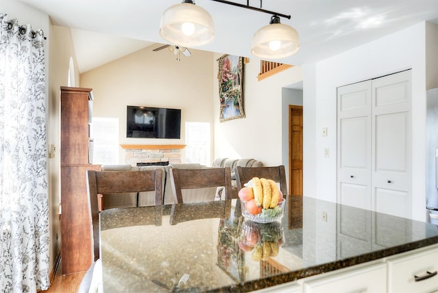 kitchen with pendant lighting, dark stone countertops, wood-type flooring, white cabinets, and vaulted ceiling