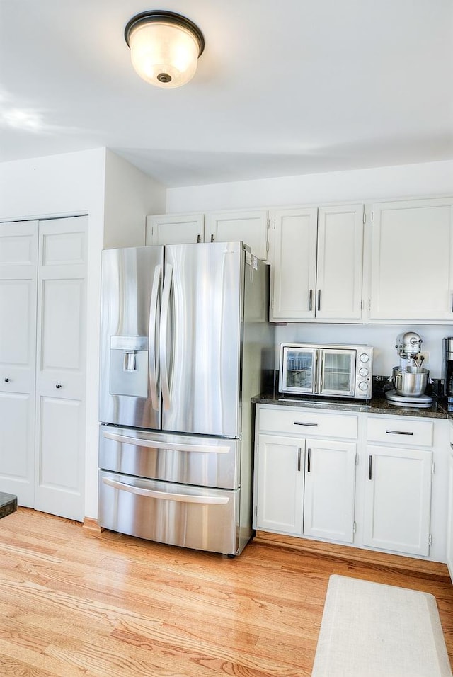 kitchen featuring white cabinetry, stainless steel fridge with ice dispenser, light hardwood / wood-style flooring, and dark stone countertops