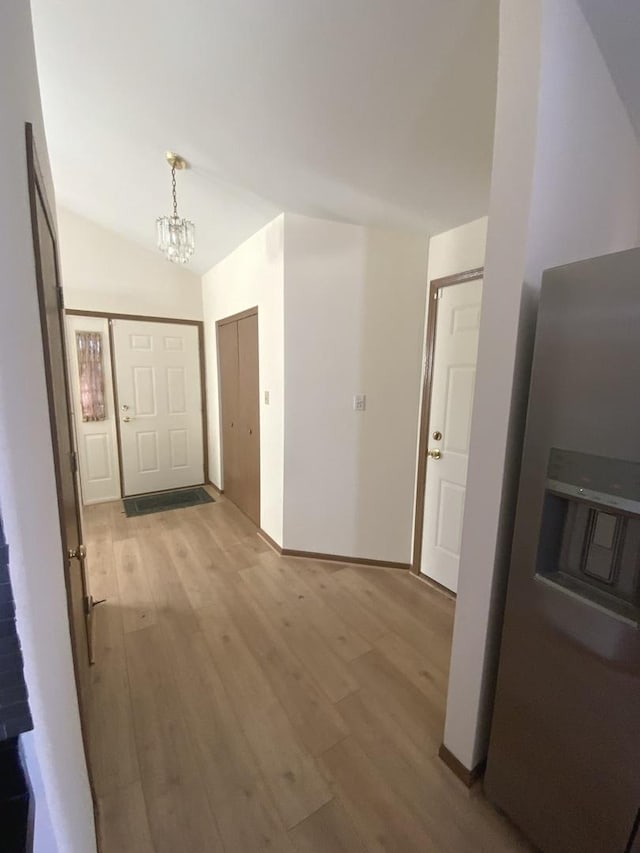 hallway featuring lofted ceiling, light hardwood / wood-style floors, and a notable chandelier