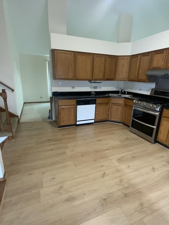 kitchen featuring a towering ceiling, dishwasher, sink, and range with two ovens