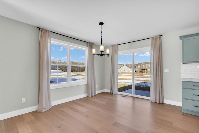 unfurnished dining area featuring an inviting chandelier and light hardwood / wood-style flooring