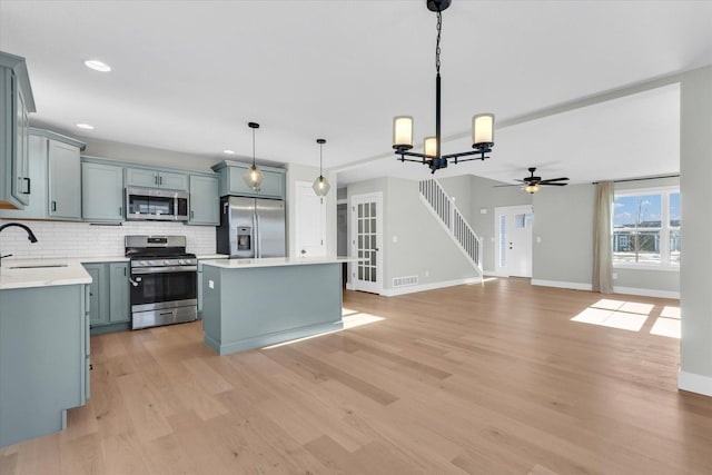 kitchen featuring sink, appliances with stainless steel finishes, backsplash, a kitchen island, and decorative light fixtures