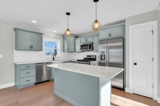 kitchen featuring sink, appliances with stainless steel finishes, a center island, light stone counters, and decorative light fixtures