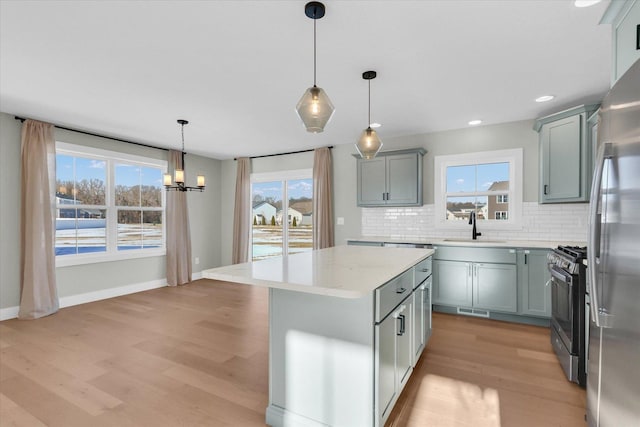 kitchen with appliances with stainless steel finishes, pendant lighting, sink, a center island, and light wood-type flooring