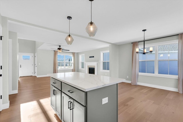 kitchen featuring gray cabinets, a kitchen island, pendant lighting, light stone counters, and light hardwood / wood-style floors