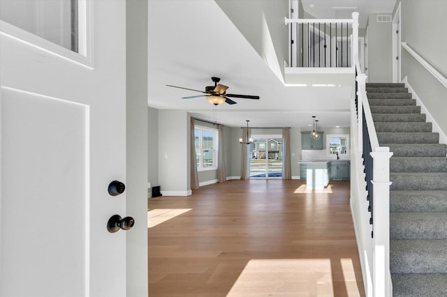 foyer with a high ceiling, wood-type flooring, and ceiling fan with notable chandelier