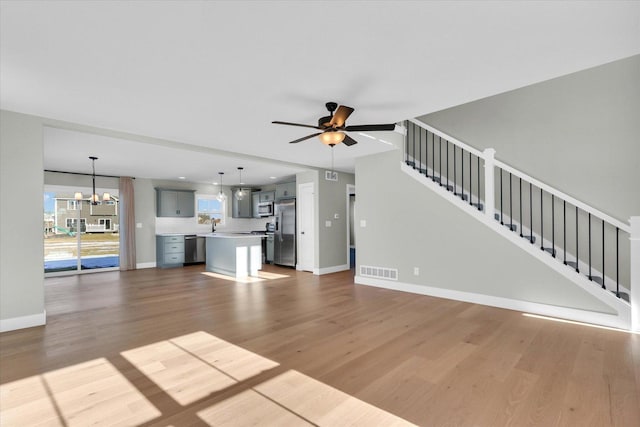 unfurnished living room featuring ceiling fan with notable chandelier and light hardwood / wood-style floors