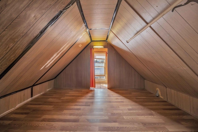 additional living space featuring wood-type flooring, lofted ceiling, and wooden walls