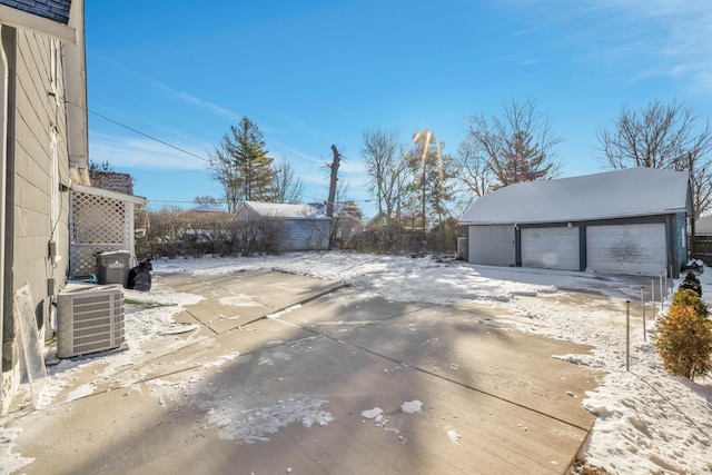 snow covered patio featuring a garage, an outdoor structure, and central air condition unit