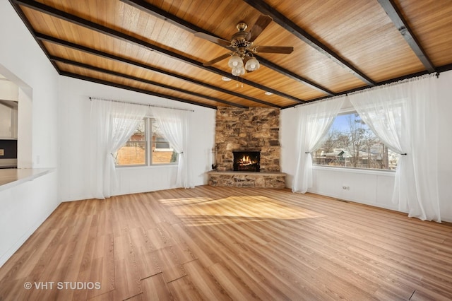 unfurnished living room featuring a stone fireplace, wooden ceiling, light wood-type flooring, ceiling fan, and beam ceiling