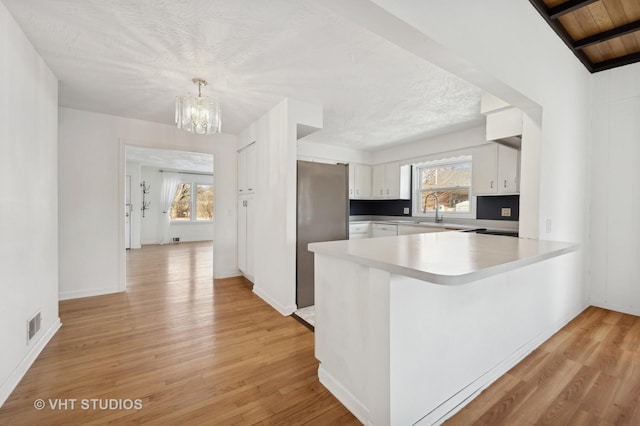 kitchen featuring pendant lighting, light hardwood / wood-style flooring, white cabinets, and kitchen peninsula