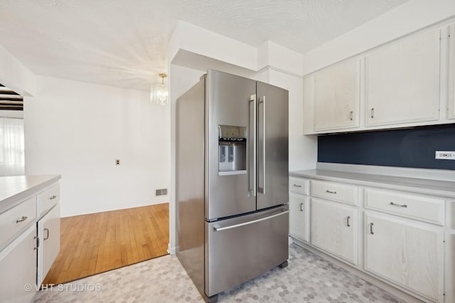 kitchen with light hardwood / wood-style flooring, a textured ceiling, hanging light fixtures, high quality fridge, and white cabinets