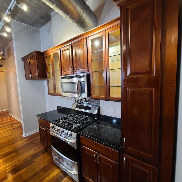 kitchen featuring appliances with stainless steel finishes, dark hardwood / wood-style flooring, and dark stone countertops