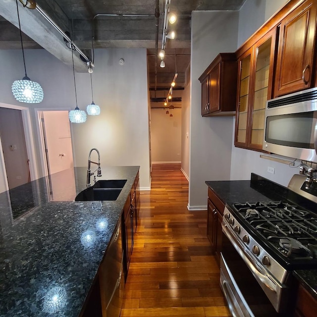 kitchen with rail lighting, sink, hanging light fixtures, dark stone countertops, and appliances with stainless steel finishes